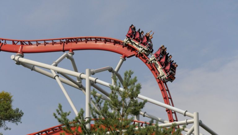 Red and white roller coaster with people having their hands up