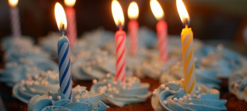 Cupcakes with blue icing with blue, yellow, and pink candles lit