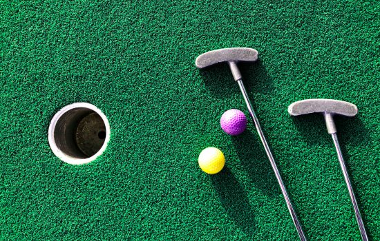 Mini golf clubs and balls on putting green background