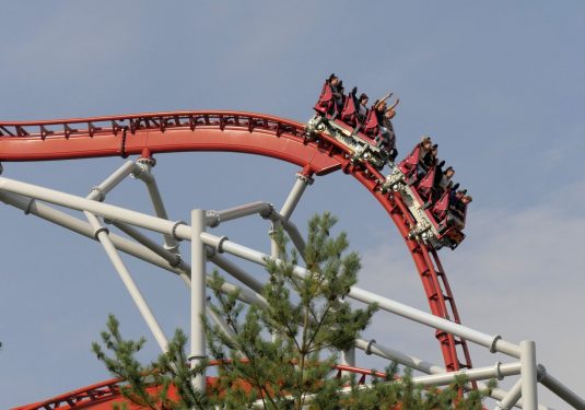 Red and white roller coaster with people having their hands up